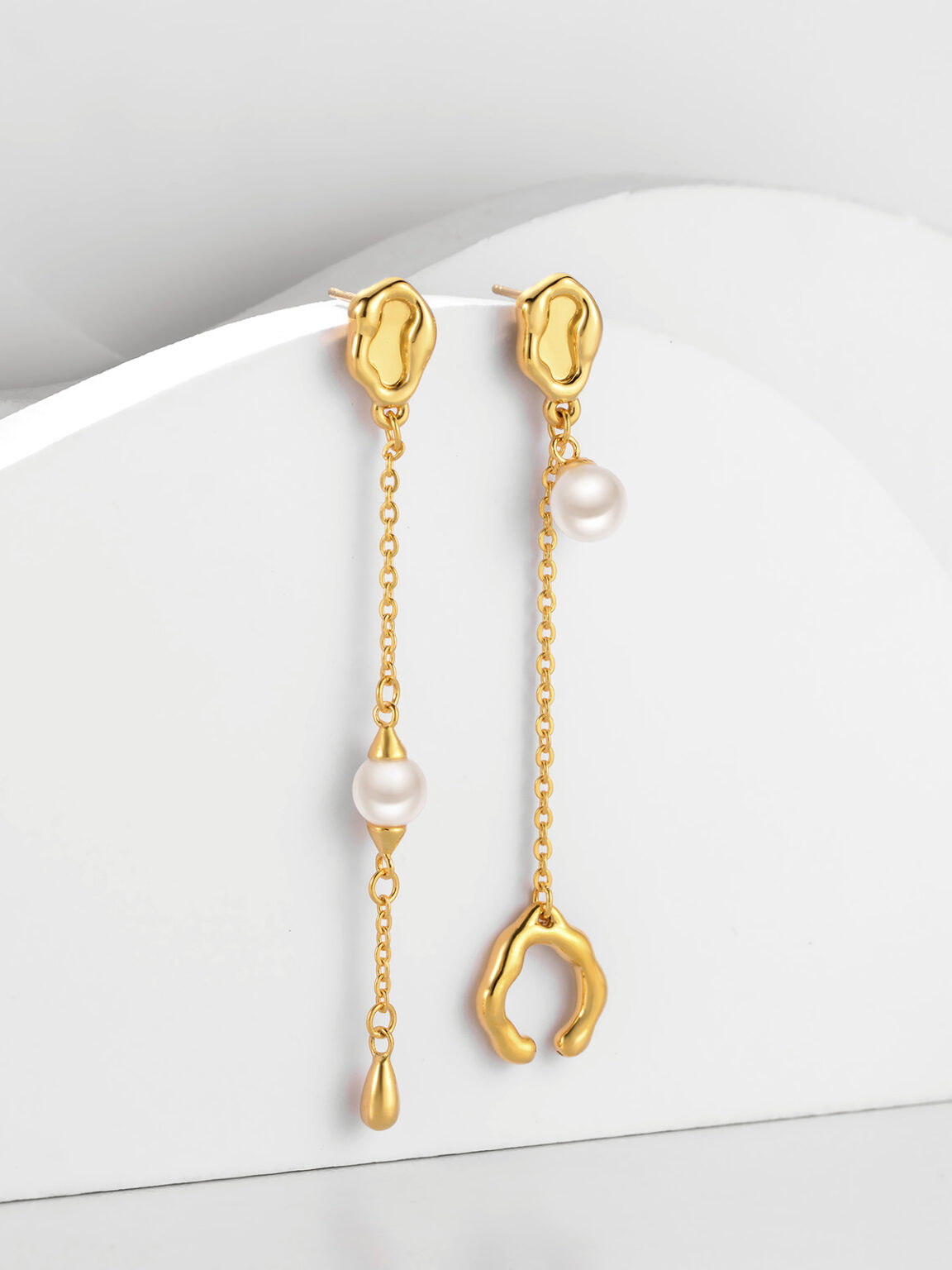 Gold pearl drop earrings photographed on a clean white curved background.