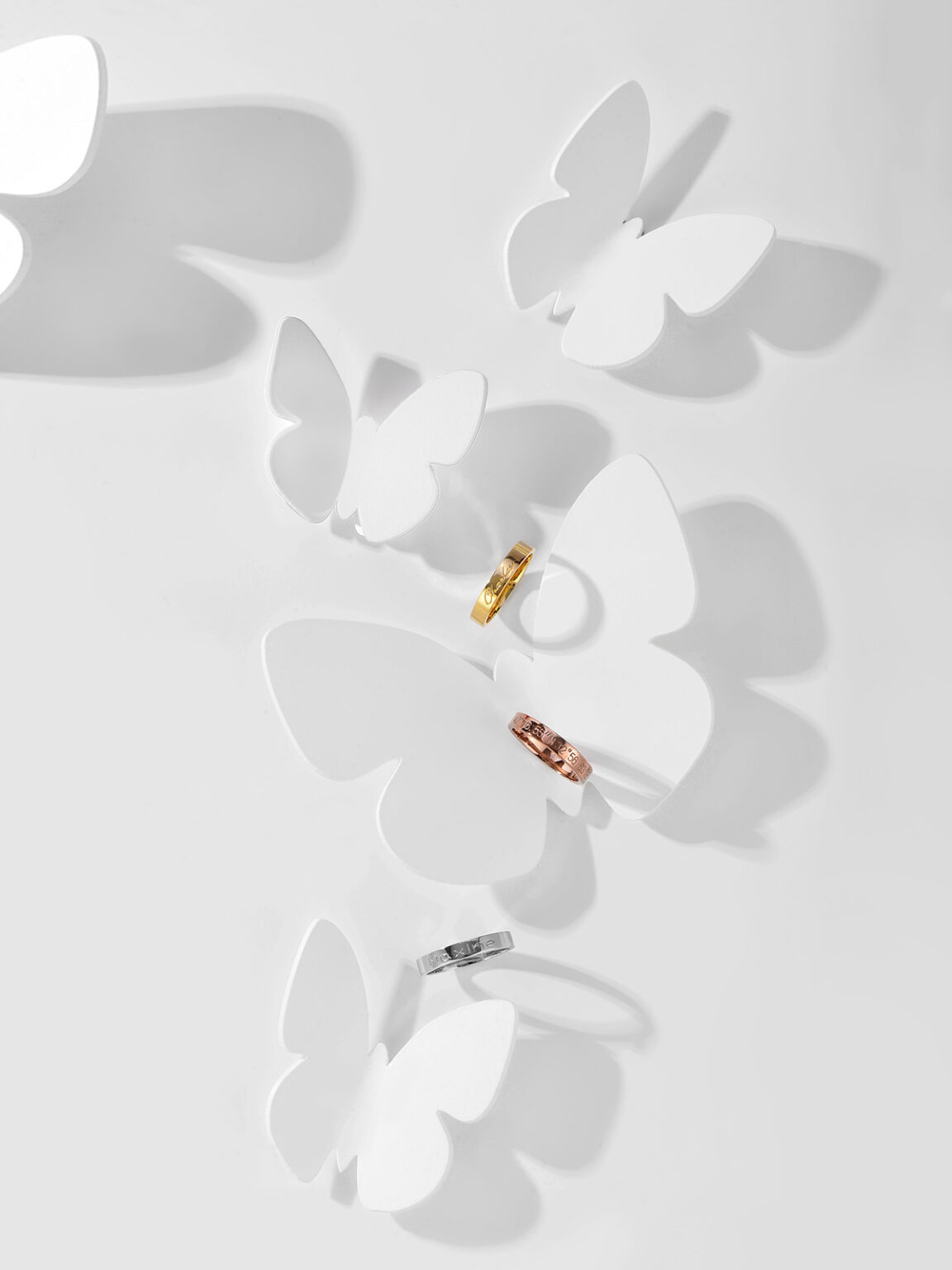 Minimalist gold earrings photographed with delicate butterfly-shaped shadows on a white background.