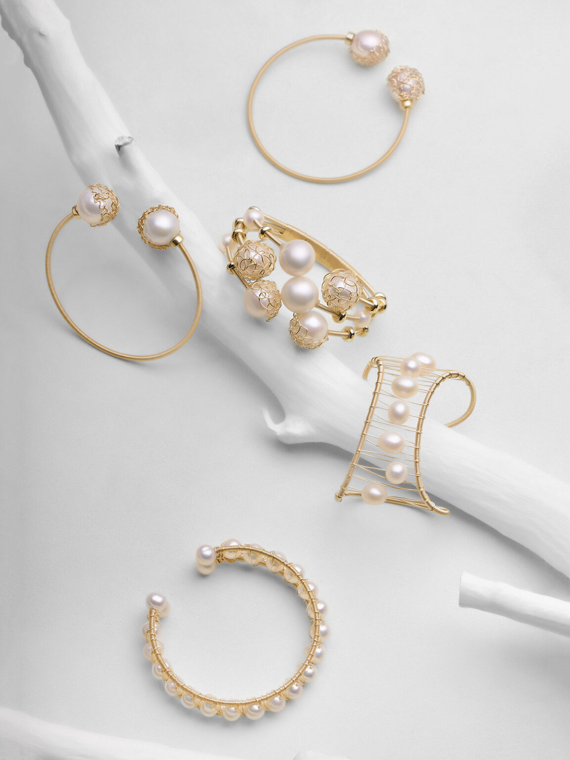 Gold pearl earrings and bracelet arranged on a soft white fabric background.