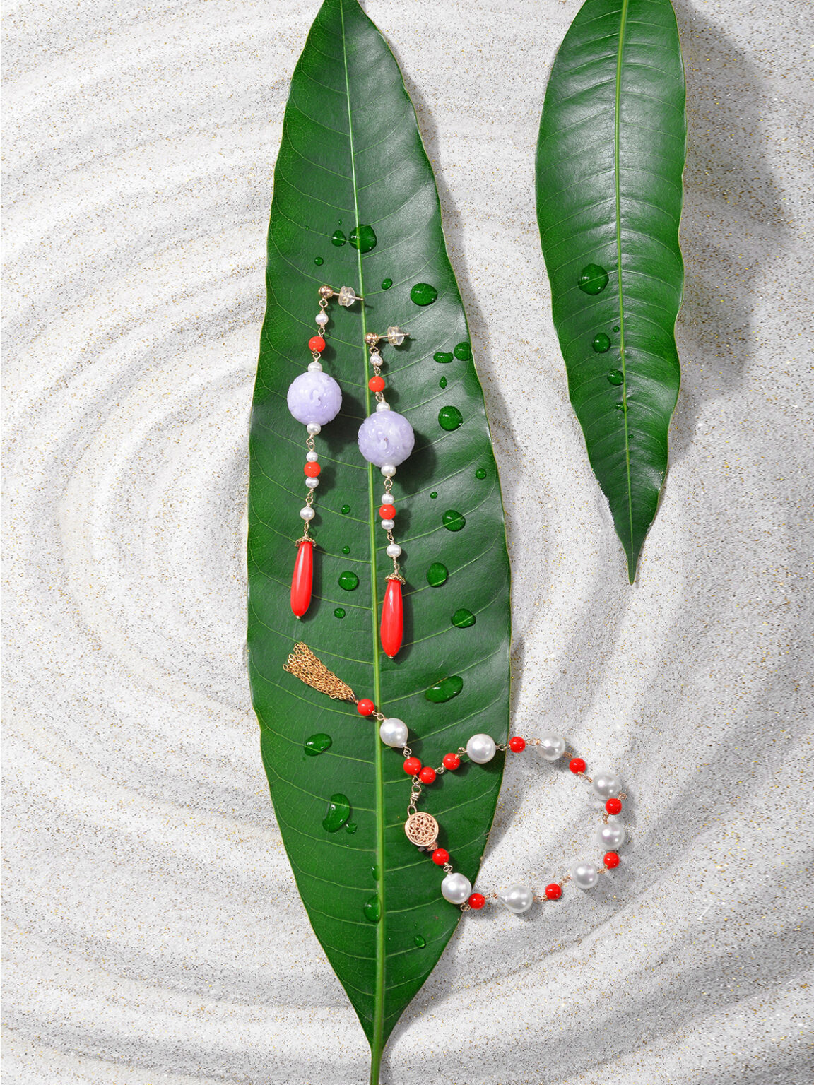 Colorful beaded jewelry arranged on green leaves and textured white fabric.