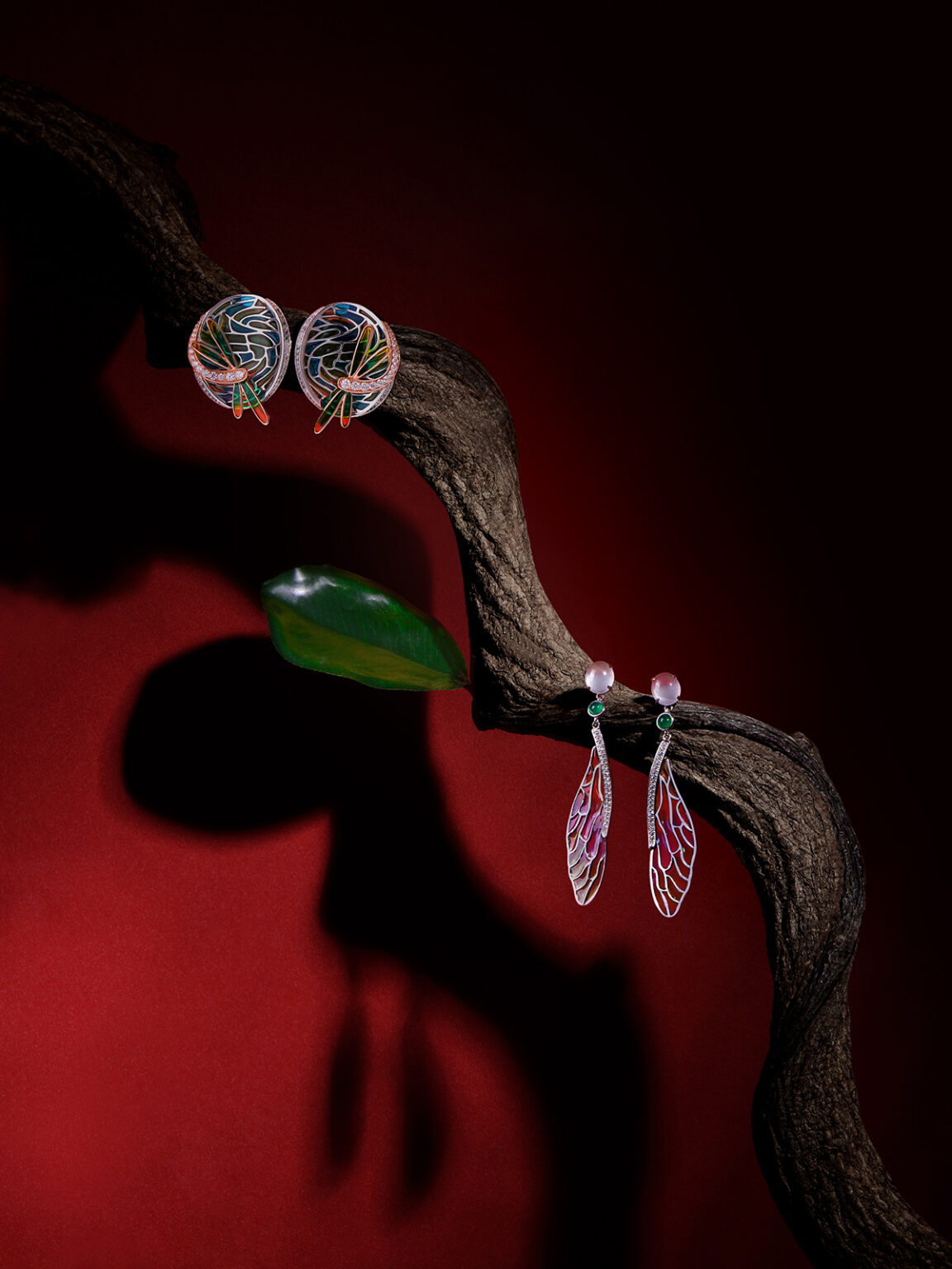 Silver gemstone drop earrings displayed on a sculptural branch against a dramatic red and black background.