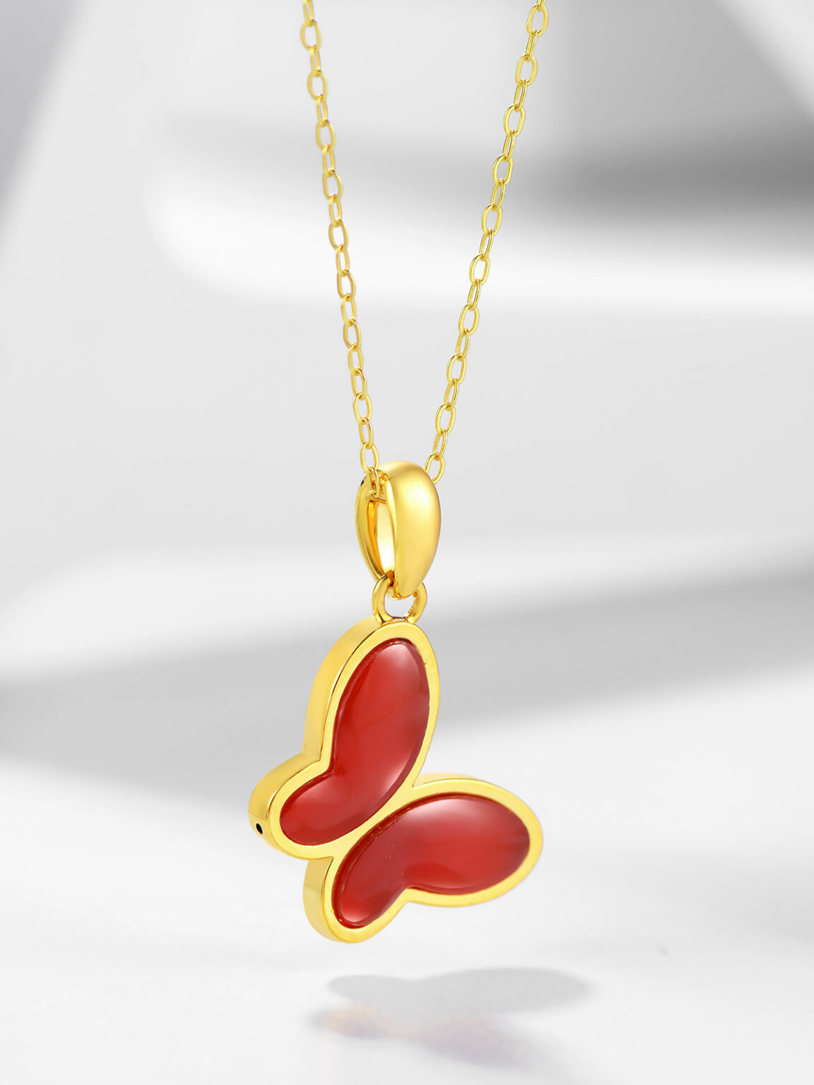 Gold necklace with a red butterfly pendant photographed on a soft white background.