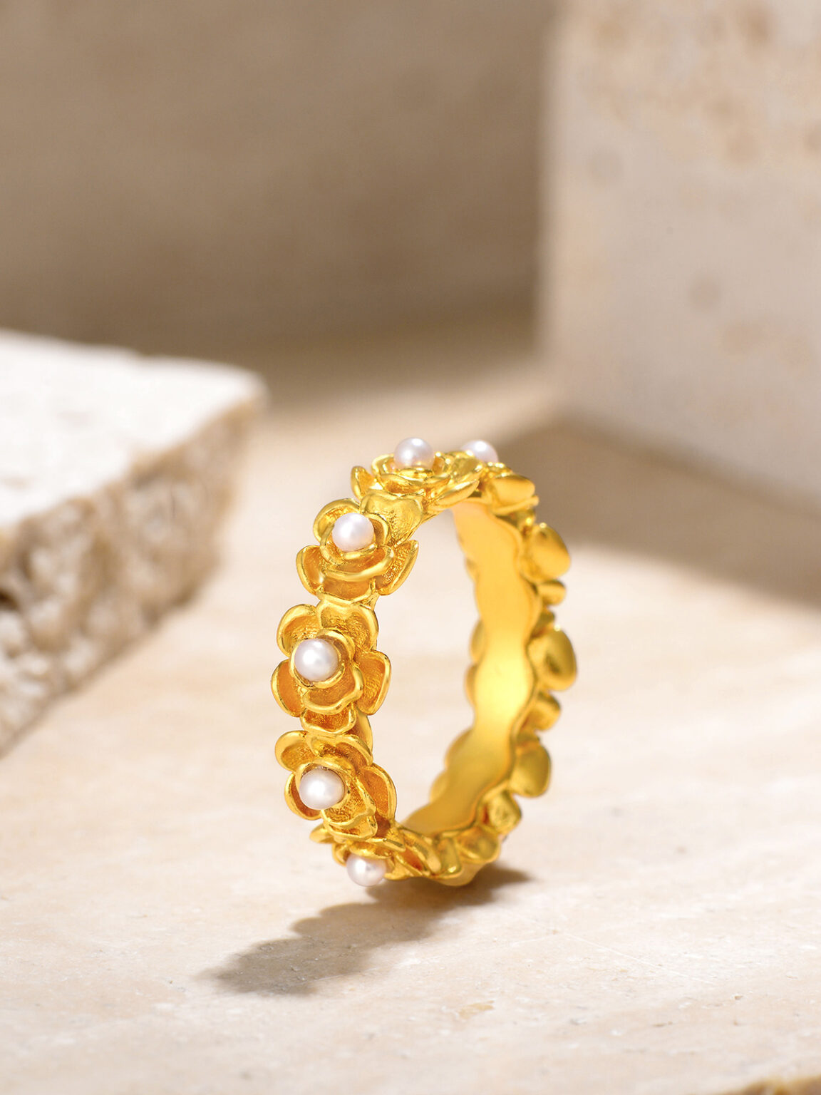 Textured gold ring photographed on a warm neutral background with soft natural shadows.