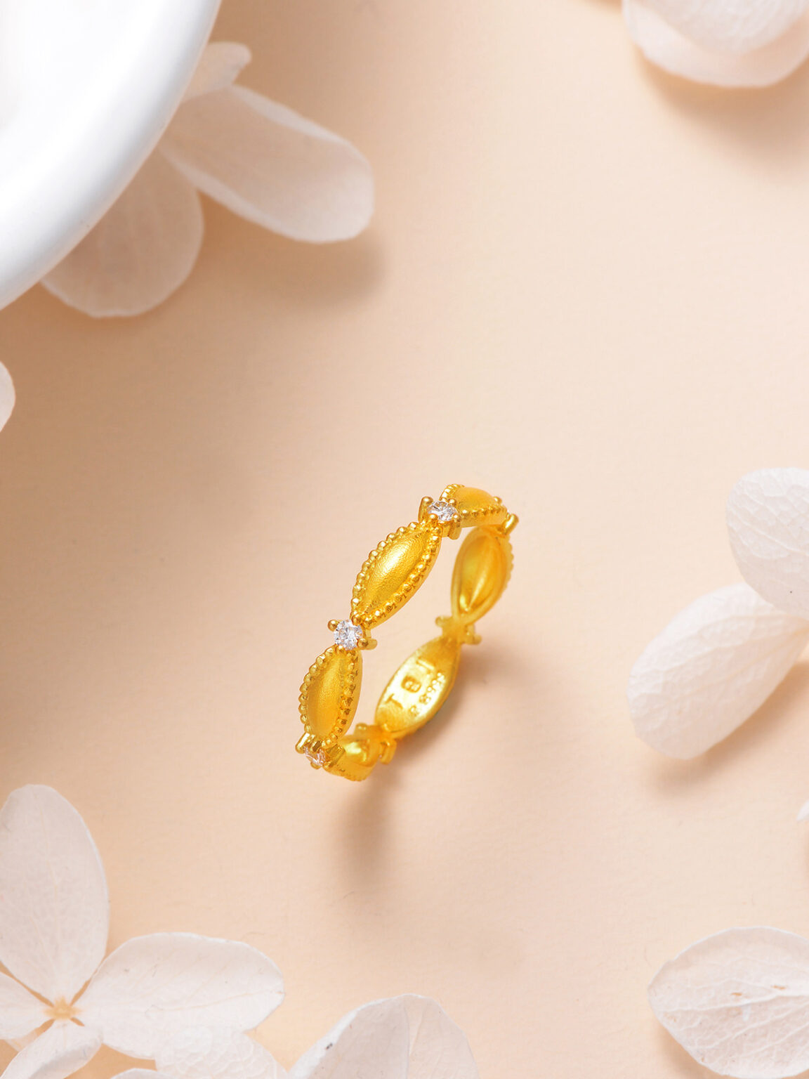 Gold ring displayed on a soft peach background with delicate white floral elements.