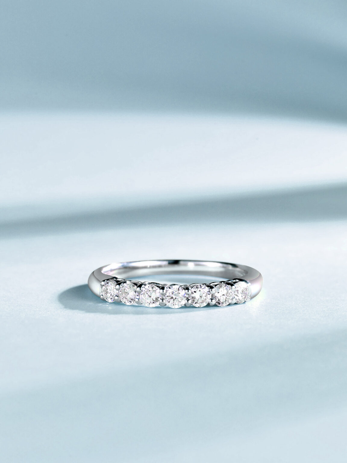 Diamond eternity ring photographed on soft blue fabric with a clean reflective finish.