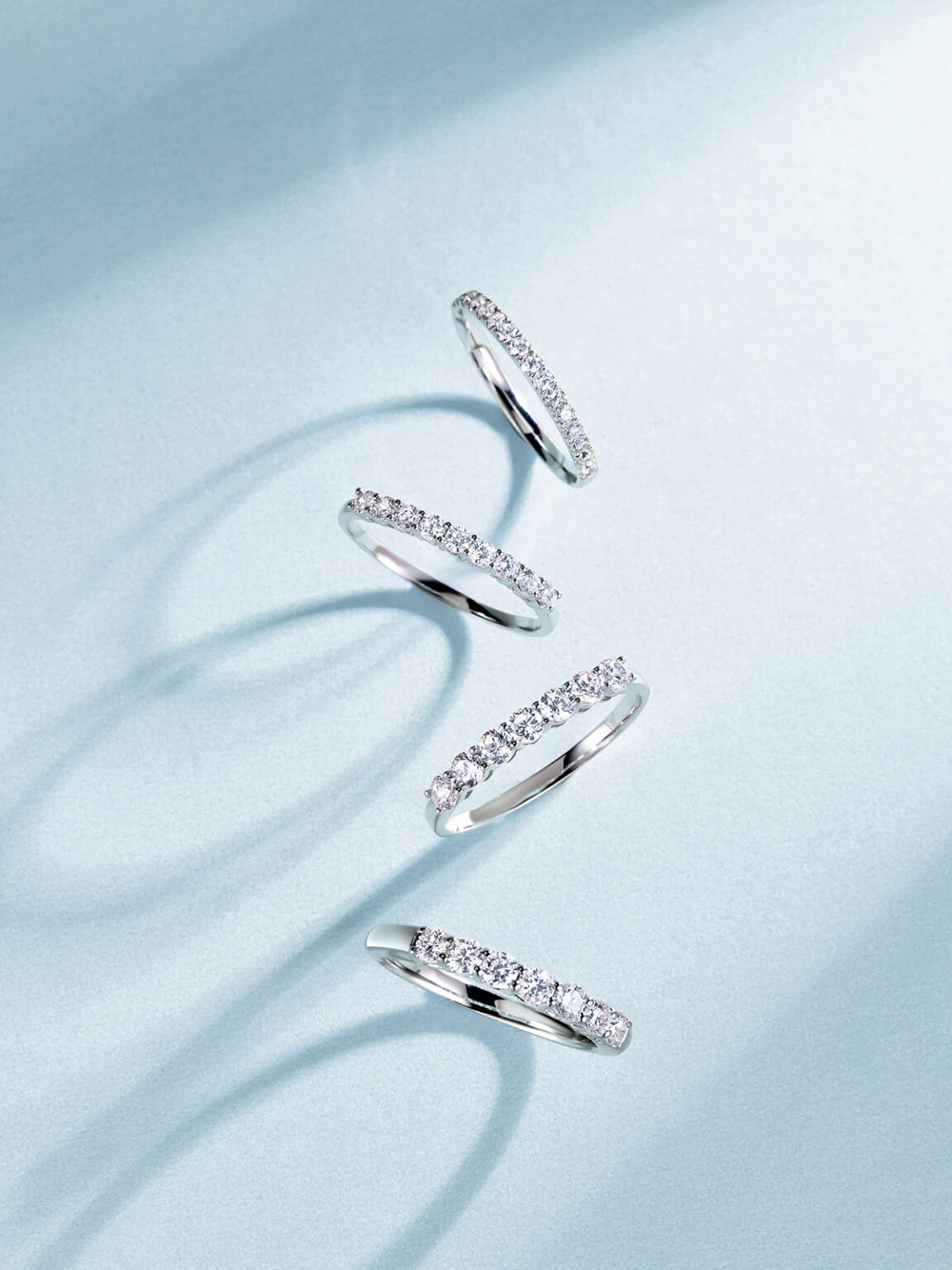 A collection of silver diamond rings arranged on flowing light blue fabric.